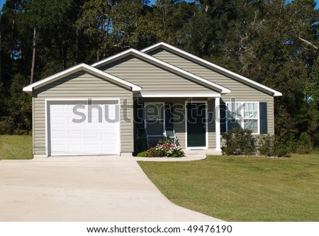 One story residential low income home with gray vinyl siding and front entry garage.