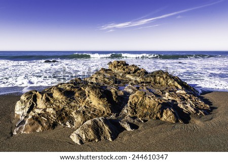 Massive rocks, blue sky and crashing waves, on Moonstone Beach, California Central Coast, near Cambria CA.