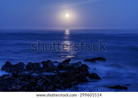 Long exposure, full moon setting, with stars, moonbeam, seafoam, back dropped on a blue sky on Moonstone Beach, along the Big Sur Highway, on the California Central Coast, near Cambria CA.