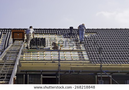 YSBRECHTUM, THE NETHERLANDS - APRIL 10, 2015: Photo of two roofers fitting tiles on renovated houses. Every worker has his own task: fitting tiles or transporting tiles  Photo taken in April 9th 2015.
