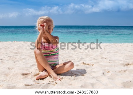 Young girl showing heart with hands and look throw it on sandy beach near by azure sea