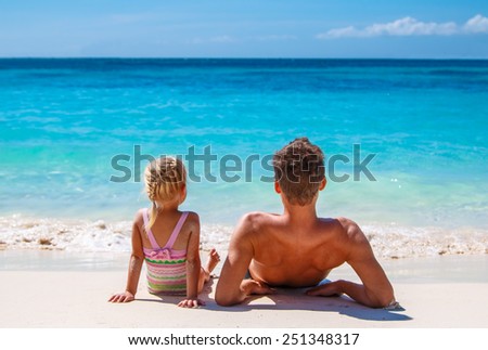 Father and daughter sitting on the beach and look at the horizon