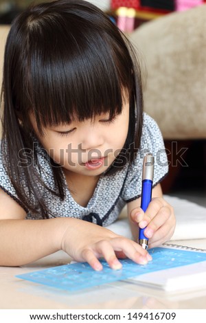 Girl lying on floor while writing using a stencil and pen