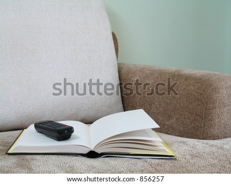 An open book with a tv remote control on a sofa couch (close-up)