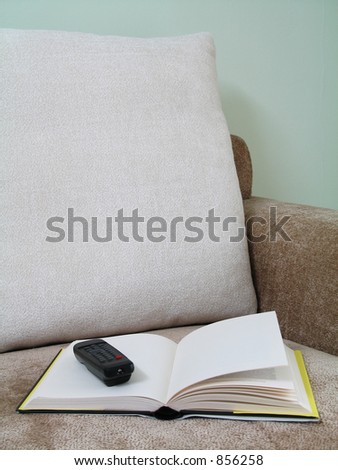 An open book with a tv remote control on a sofa couch (vertical)