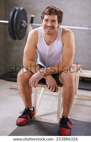 Handsome young man sitting on a bench in his private gym smiling