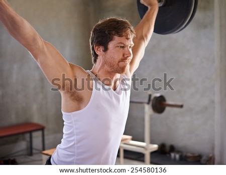Strong man looking fiercely determined while lifting heavy weights in a private gym