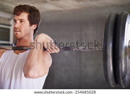 Handsome young man with strong physique lifting heavy weights in a private gym