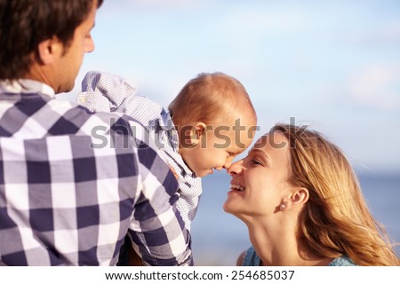 Baby boy leaning over his dad\'s shoulder to playfully touch noses with his beautiful smiling mother