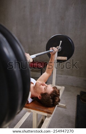 Young man lifiting weights while lying down in a private gym, with copyspace
