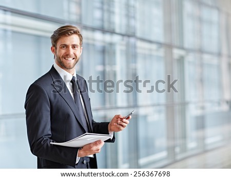 Corporate executive smiling at the camera while holding his phone and a notes