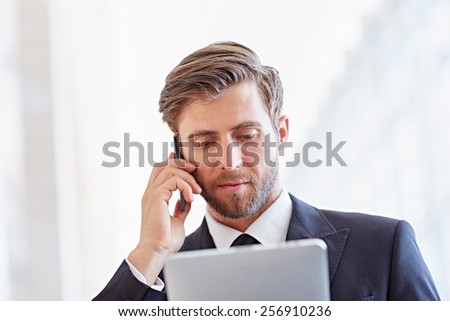 Closeup of a serious corporate executive listening on his phone while looking at a digital tablet
