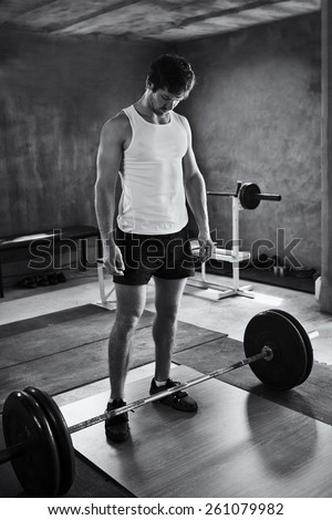 Black and white image of a strong young man looking quietly at the weights he is about to lift
