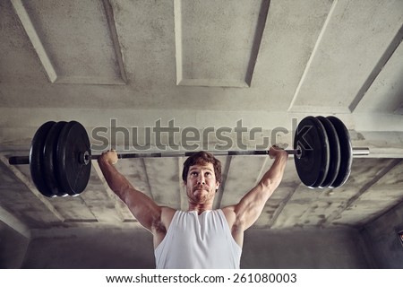 Low angle shot of a strong young man lifting heavy weigths above his head with a determined expression