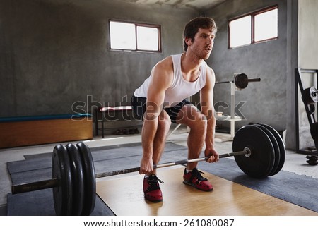 Wide angle image of a serious young man about to lift some heavy weights in a private gym