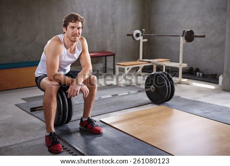 Handsome young man sitting on wieghts looking at the camera in a private gym