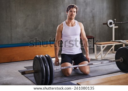 Fit personal trainer kneeling behind his weightlifting equipment in a private gym