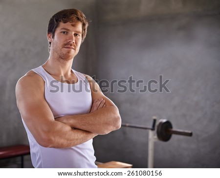 Handsome young man with strong physique looking confidently at the camera with weigthlifting equipment in the background