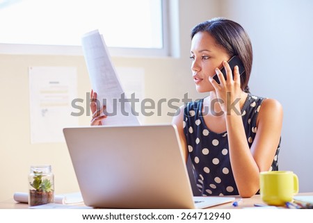 A young businesswoman talking on the phone while looking at a document