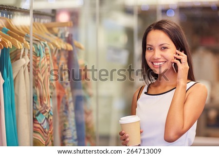A young woman talking on the phone while browsing for clothes in a shop