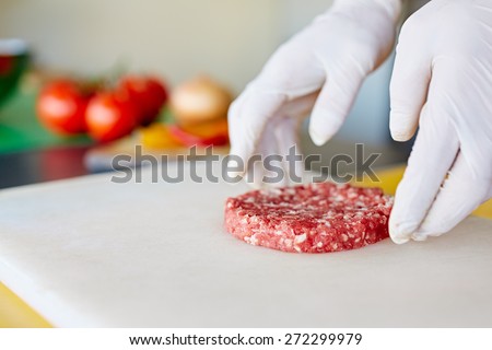 Cropped image of hands wearing white latex gloves preparing a hamburger patty in a clean and hygeinic environment