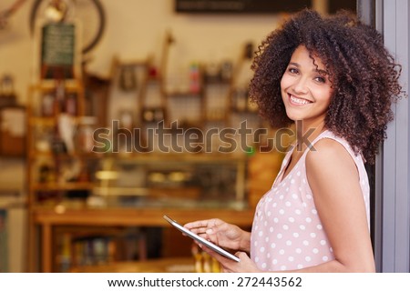 Beautiful mixed race woman with an afro hairstyle holding a digital tablet while standing in the doorway of her coffee shop