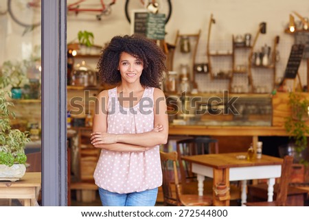 Beautiful young cafe owner proud of her small business standing smiling in the doorway of her coffee shop