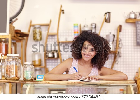Beautiful young mixed race woman in her coffee shop writing out an order on the counter