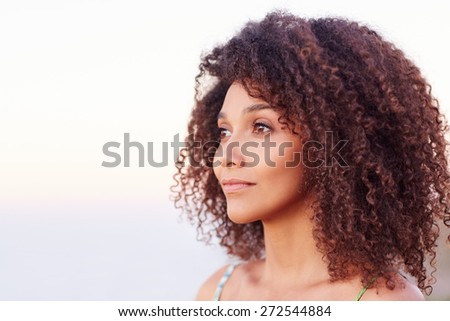 Beautiful mixed race woman with curly afro hair looking serenely away outdoors