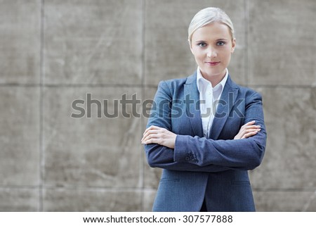 A young businesswoman with her arms folded on grey textured background
