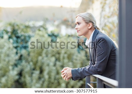A young businesswoman leaning against the railing of her office balcony