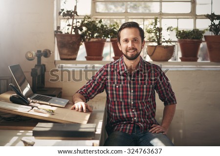 Young male entrepreneur sitting in the office space of his design studio looking confidently at the camera