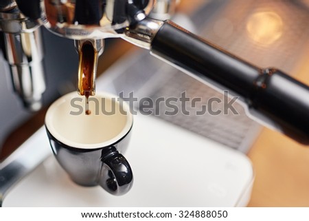 High angle shot of a drop of fresh coffee falling from the spout of a coffee machine espresso dispenser into a clean ceramic cup