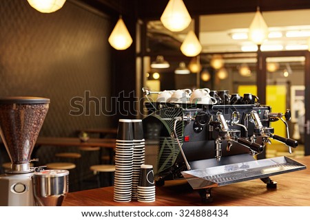 Hipster looking coffee shop ready to open for the day with a clean and tidy counter and well-maintained shiny coffee machine on the the wooden surface
