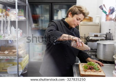 A female chef drizzling balsamic vinegar on an open sandwich