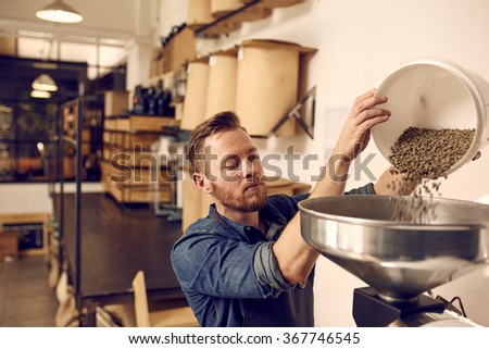Entrepreneur pouring raw coffee beans into a modern roasting mac