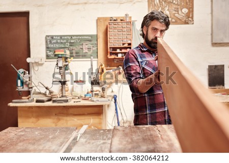 Expert carpenter in his workshop, looking down the length of a wooden plank, checking it for quality and straightness