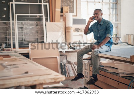 Handsome African designer talking on phone in his studio