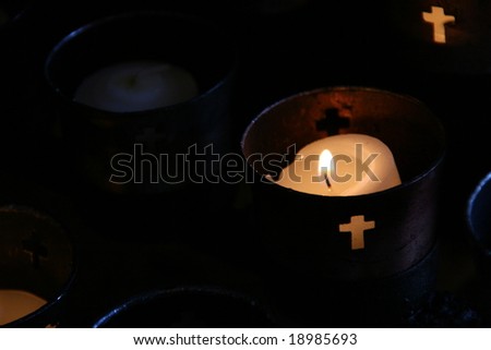 small votive candles burning in religious cups with cross cutouts
