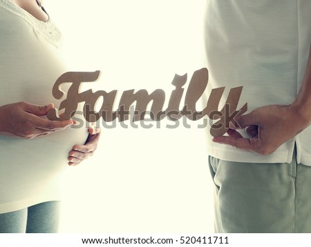 Pregnant woman with husband holding family message for incoming baby isolated on white background. Concept for baby shower and warm family.
