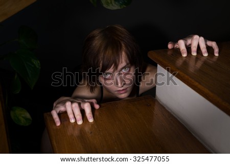 Evil zombie girl with glowing eyes crawling to you from under the stairs