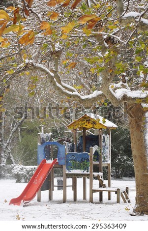 Red slide and wooden house in the park covered with snow.