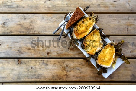 Three oysters cooked under parmesan in a plate on a rough wooden table