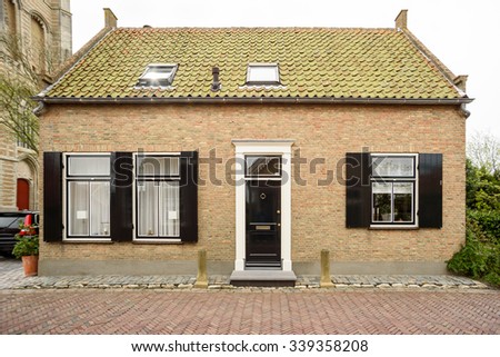 A typical dutch house with a tiled roof, black door and shutters on the windows
