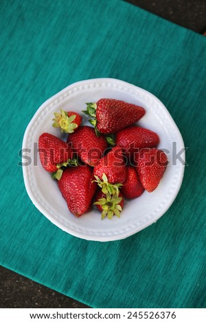 A bowl of fresh strawberries against a teal background