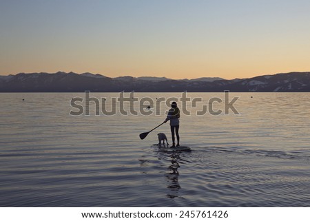 A woman paddles on a SUP board with a dog on a lake