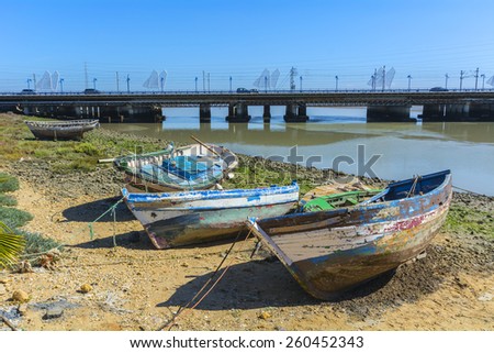 Old fishing boats on the shore of a river, with a bridge in the background