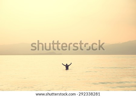 Man into water with hand raised breath at sunset