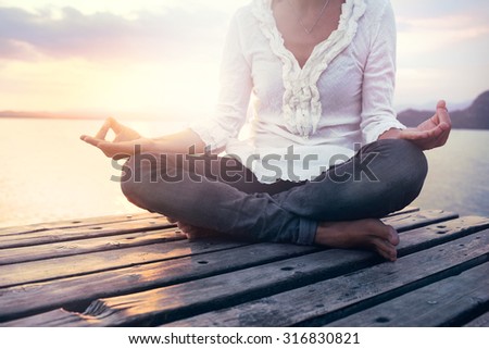 beautiful woman meditating on a boardwalk at sunset