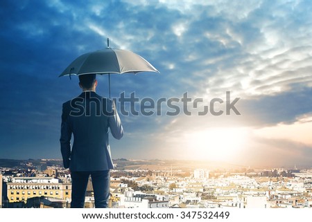 Business man with umbrella observing the sunset on the city